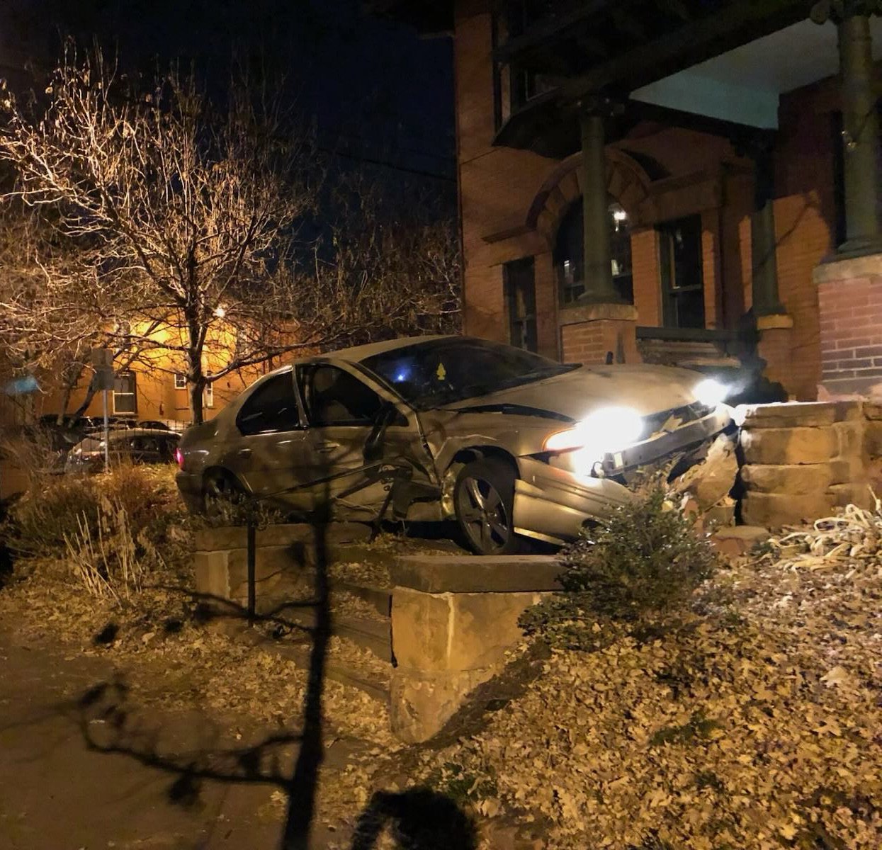 A heavily damaged car resting in the front yard of a home after a nighttime crash