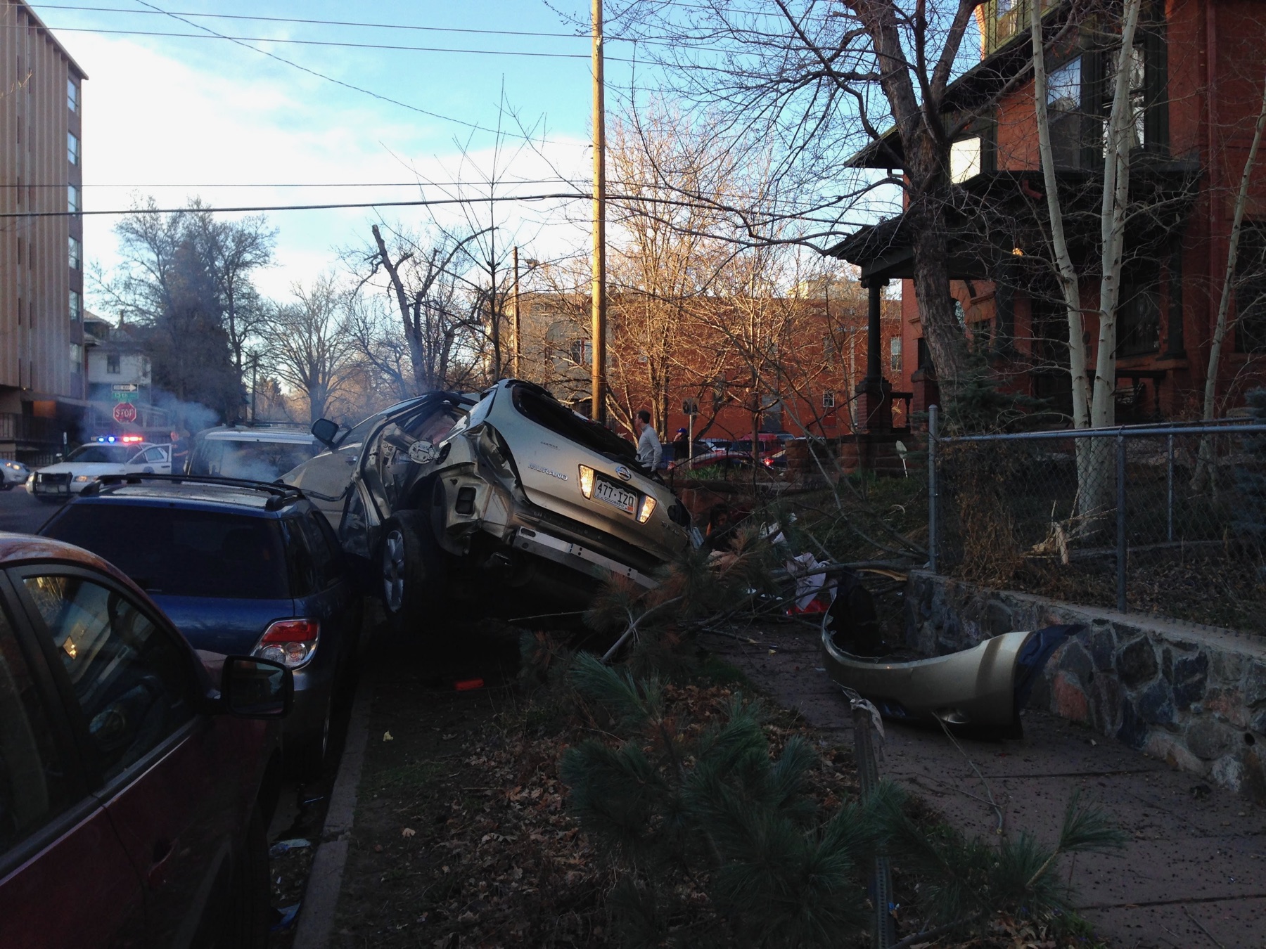 A crashed SUV lifted over parked cars beside an East Avenue sidewalk